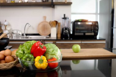 Cam bardakta renkli taze sebze salatası ve mutfak tezgahında yemek malzemeleri, güzel modern mutfağın bulanık arka planı, fotokopi alanı olan sağlıklı doğal gıda konsepti..