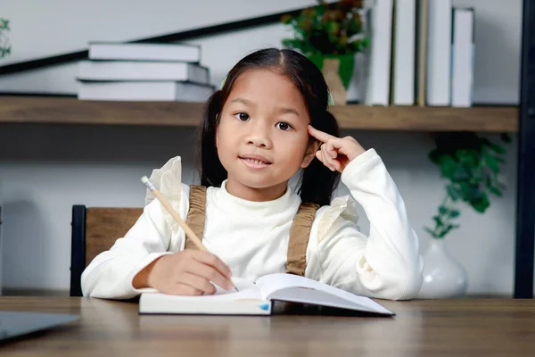 亚洲可爱的小女孩在想她的功课 女学生在家里学习和做作业 快乐的孩子在笔记本里学习和写作 孩子教育 — 图库照片