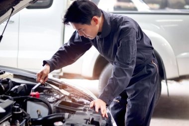 Asyalı yakışıklı tamirci motorlu araçla çalışıyor. Otomobil tamircisi. Garaj tamir atölyesinde müşteri otomobili bakım motoru sistemini inceliyor..