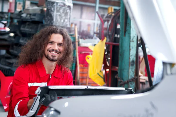 Kırmızı Üniformalı Uzun Saçlı Yakışıklı Tamirci Otomobil Tamirhanesinde Çalışıyor Otomobil — Stok fotoğraf