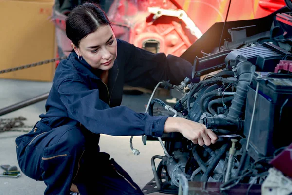 Beautiful female auto mechanic in uniform working with engine vehicle at garage, car service technician woman checking and repairing customer car at automobile service center, vehicle repair service.