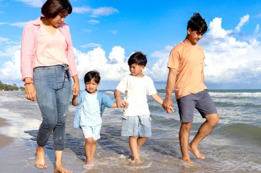 Mutlu aile, yaz tatilinde birlikte vakit geçirir. Neşeli ebeveynler ve çocuklar el ele tutuşur ve mavi gökyüzüyle sahilde yürüyüş yapar. Aile, kumsalda rahatlatıcı bir hafta sonu geçirir..