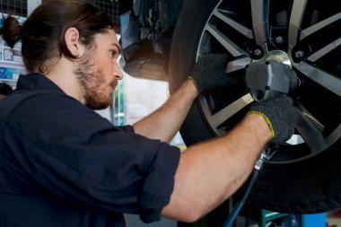 Otomobil tamircisi yakışıklı adam garajda tekerlek lastiklerini kontrol ediyor, araba servisi teknisyeni otomobil tamirhanesinde müşteri arabasını kontrol ediyor ve tamir ediyor, araba tamirhanesi işletiyor..