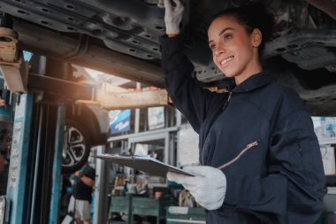 Güzel kadın otomobil tamircisi garajda tekerlekleri kontrol ediyor, araba servisi teknisyeni kadın otomobil servisinde müşteri arabasını tamir ediyor, aracın altını ve süspansiyon motor sistemini denetliyor..