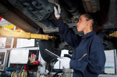 Güzel kadın otomobil tamircisi garajda tekerlekleri kontrol ediyor, araba servisi teknisyeni kadın otomobil servisinde müşteri arabasını tamir ediyor, aracın altını ve süspansiyon motor sistemini denetliyor..