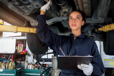 Güzel kadın otomobil tamircisi garajda tekerlekleri kontrol ediyor, araba servisi teknisyeni kadın otomobil servisinde müşteri arabasını tamir ediyor, aracın altını ve süspansiyon motor sistemini denetliyor..