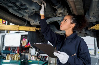 Güzel kadın otomobil tamircisi garajda tekerlekleri kontrol ediyor, araba servisi teknisyeni kadın otomobil servisinde müşteri arabasını tamir ediyor, aracın altını ve süspansiyon motor sistemini denetliyor..