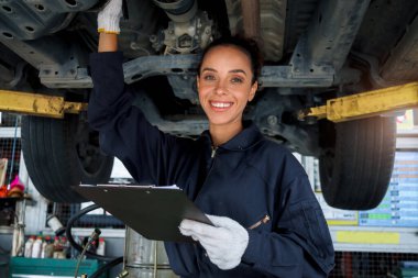 Güzel kadın otomobil tamircisi garajda tekerlekleri kontrol ediyor, araba servisi teknisyeni kadın otomobil servisinde müşteri arabasını tamir ediyor, aracın altını ve süspansiyon motor sistemini denetliyor..