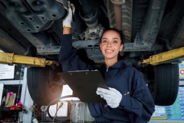 Güzel kadın otomobil tamircisi garajda tekerlekleri kontrol ediyor, araba servisi teknisyeni kadın otomobil servisinde müşteri arabasını tamir ediyor, aracın altını ve süspansiyon motor sistemini denetliyor..