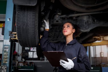 Güzel kadın otomobil tamircisi garajda tekerlekleri kontrol ediyor, araba servisi teknisyeni kadın otomobil servisinde müşteri arabasını tamir ediyor, aracın altını ve süspansiyon motor sistemini denetliyor..