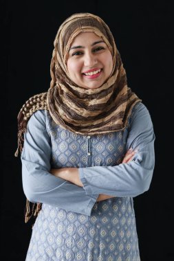 Orta yaşlı gülümseyen güzel bir Asyalı Müslüman kadının portresi başörtüsü ve geleneksel kostüm giyiyor, koyu siyah arka planda kolları bağlı duruyor..