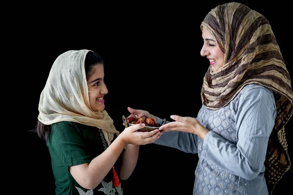 Beautiful Asian Muslim woman with daughter girl wear hijab scarf and traditional costume, hold date fruits together, sweet and energy boost food mostly eat in Ramadan of Islam on dark black background