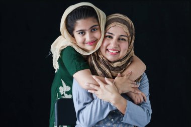 Mutlu gülümseyen, güzel gözlü, tesettürlü Müslüman bir kız. Annesine sarılan geleneksel bir eşarp takıyor. Anne ve kızının sıcak sevgisi..