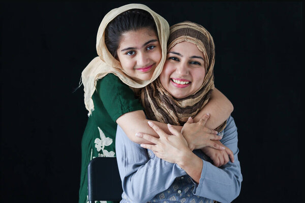 Счастливая улыбающаяся мусульманская девушка с красивыми глазами носить хиджаб шарф и традиционный костюм объятия с матерью, теплой любви в семье мамы и дочери, прекрасная исламская семья на темном черном фоне.