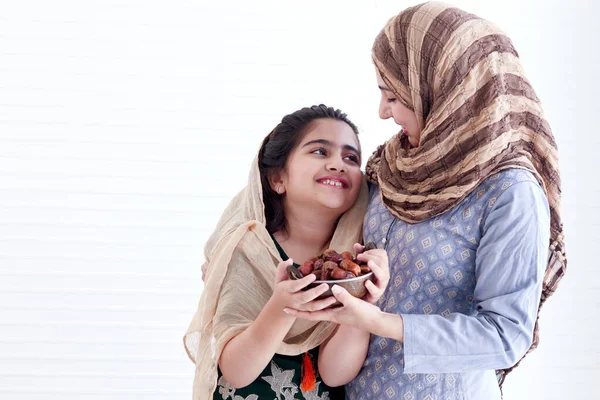 Beautiful Asian Muslim woman with daughter girl wear hijab scarf and traditional costume, hug each other, hold date fruits together, sweet food eating in Ramadan of Islam on white background.