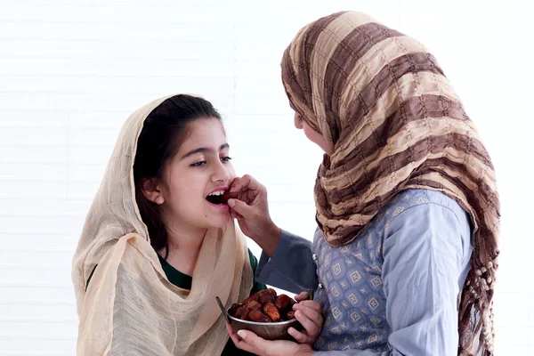 Asian Muslim family, woman and kid wear hijab scarf and traditional costume, daughter girl enjoy eating date fruits with mother hand, sweet Islamic halal food eat in Ramadan of Islam, mom feed child.