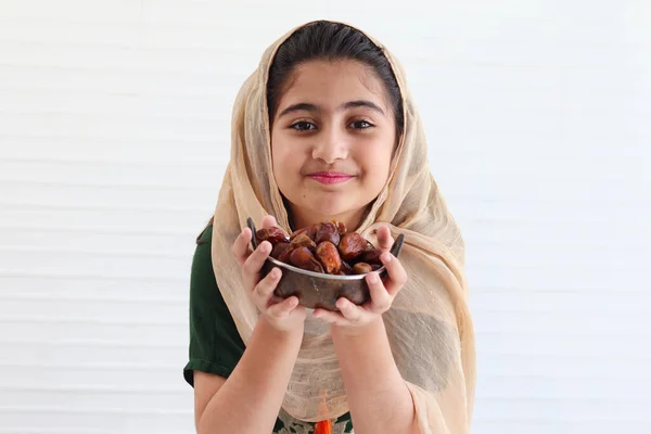 幸せな笑みを浮かべてパキスタンのイスラム教徒の少女は美しい目をヒジャーブと伝統的な衣装を着て 日付の果物を保持 白を背景にイスラム教のラマダーン月で甘い食べ物を食べる肖像インドの子供 — ストック写真