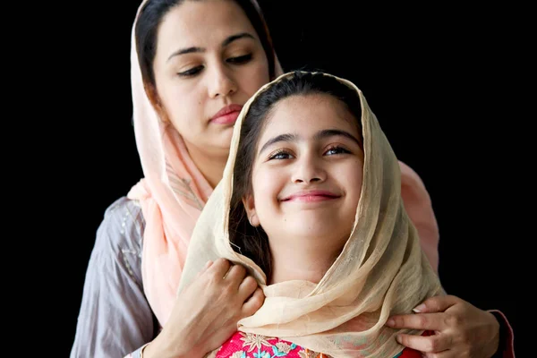 可愛いです笑顔の肖像パキスタンのイスラム教徒の女の子で美しい目と彼女の母親身に着けていますヒジャーブ伝統的なドレスで暗い黒の背景 暖かい愛で幸せなイスラム教徒の家族の母と娘 — ストック写真