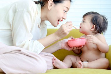 Anne, küçük tatlı bir kızı besler sarı bir kanepede bebek gibi yürür, bebek, anne için sağlıklı ev yemekleri yemekten hoşlanır, ebeveyn, aile içinde çocuğa bakar..