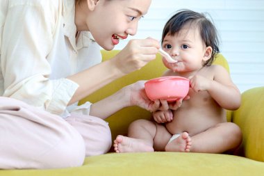 Anne, küçük tatlı bir kızı besler sarı bir kanepede bebek gibi yürür, bebek, anne için sağlıklı ev yemekleri yemekten hoşlanır, ebeveyn, aile içinde çocuğa bakar..