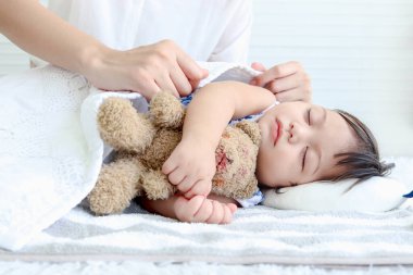 Beyaz yatakta uyuyan tatlı bebek bebek, uykulu küçük kızı battaniyeyle örten anne elleri, uyuyan çocuğu rahatlatan anne, evde bakıcı çocuk, aileyi seven aile..