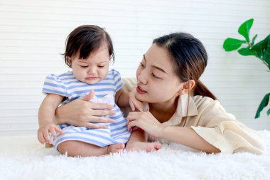 Mutlu bebek bebek ve anne oturma odasında pofuduk beyaz halı döşemesine oturur, küçük kız ve anne oyuncaklarla oynar, ebeveynler çocuğa bakar, evde bebeğe bakar, ailede aşık olur..