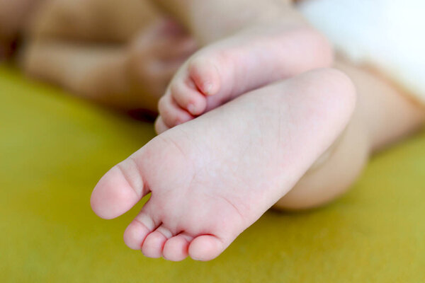 Закройте крошечные босые милые ноги новорожденной девочки на желтой кровати, маленькие младенческие ноги, счастливая семья и концепция детства, прекрасный момент зачатия ребенка.