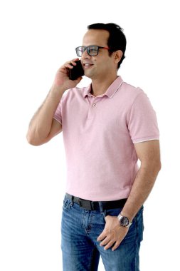 Orta yaşlı mutlu Hintli bir adamın portresi pembe tişörtlü, gözlüklü, ayakta duran ve cep telefonuyla konuşan, beyaz arka planda izole edilmiş, kendine güvenen Asyalı erkek cep telefonu tutan.