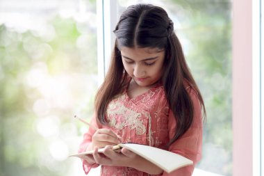 Uzun saçlı, geleneksel kıyafet kostümü giyen Hintli öğrenci kız öğrenci kütüphanede ödev yapmak için defter ve kalem tutuyor, Asyalı kadın çocuk eğitimi alıyor..