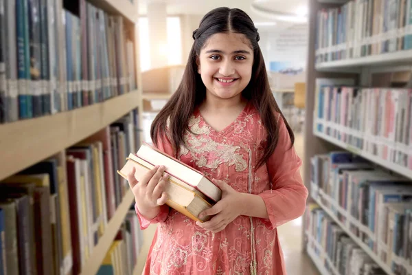 伝統的な衣装を着て長い髪の美しい目を持つ幸せな笑顔インドの学校の女の子の肖像画は 図書館で本を保持し 学生の子供は本棚の近くに立っています アジア系女子教育 — ストック写真