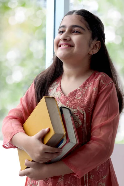 幸せな笑顔の肖像長い髪と伝統的なドレスの衣装を身に着けている美しい目を持つインドの学校の女の子 図書館の窓の近くに本を保持しています 教育とアジアの女性の学生の子供の子供 — ストック写真