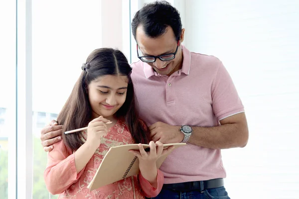 可爱的印度女学生穿着传统衣服在窗边 拿着笔记本铅笔做作业 父亲在家里教女儿 父母参与家庭教育 — 图库照片