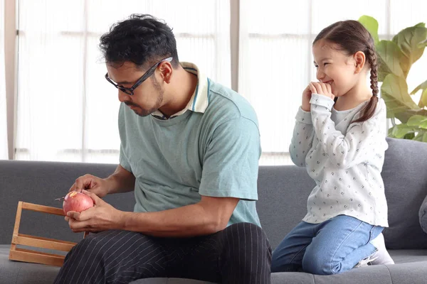 英俊的爸爸为女儿剥苹果 可爱的小女孩坐在客厅的沙发上 等着吃苹果 可爱的家人在一起 父亲照顾孩子 父亲节快乐 — 图库照片