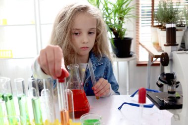 Uzun sarı saçlı ilkokul kızı laboratuvarda kimya bilimi deneyi yapıyor. Renkli test tüpleri ve laboratuvar ekipmanları olan sevimli bilim adamı çocuk sınıfta biyoloji ve kimya öğreniyor..