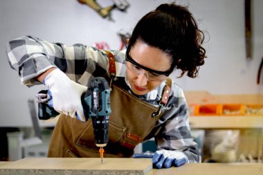 Ahşap kalasları ölçmek için sarı mezura tutan genç marangoz kadın, ahşap atölyesinde ahşap mobilya yapan kadın, marangoz dükkanında çalışan kadın..