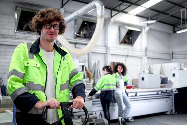 快乐微笑的年轻工人 留着卷曲的头发 戴着眼镜和安全背心 在工厂工作 工业男性工程师拖曳交通工具 工人在工作场所工作 — 图库照片