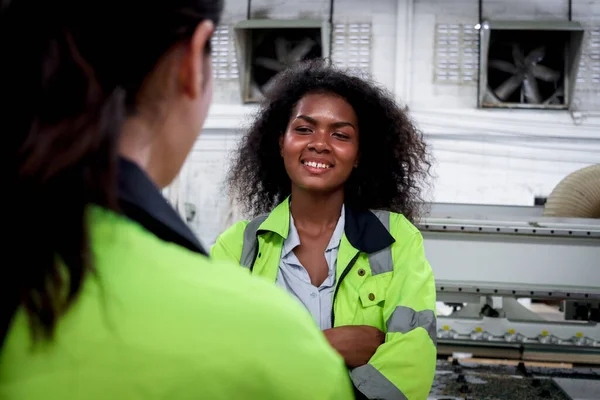 快乐的微笑着的非洲女工 卷曲的头发和同事在工厂里交谈 穿着安全背心的工业女工程师和同事一起在建筑工地工作 — 图库照片