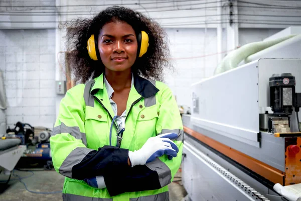 穿着安全背心和防护耳机 头戴卷发的快乐的非洲女工业工人的画像 他们手挽手站在Cnc木材厂旁 工作场所的女工程师 — 图库照片