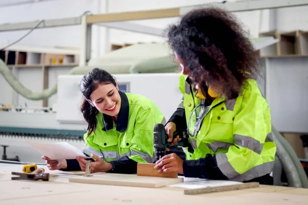 穿着安全背心的工业漂亮女工持图 与手钻工艺的非洲卷发女工讨论 在Cnc木工家具厂一起工作 — 图库照片