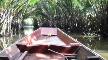Tayland 'ın eski ahşap teknesinin önünde kanal suyu üzerinde yüzüyor ve Tayland' ın Surat şehrinde Nipa palmiyesi yeşil ağaç tünelinde ilerliyor..