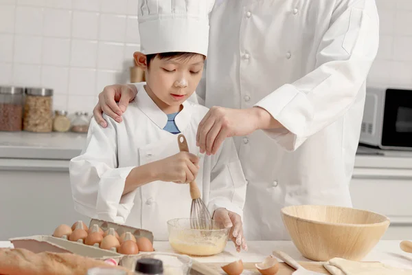 快乐的亚洲儿子和父亲 身穿厨师制服 头戴帽子 一起在厨房做饭 父亲和儿子一起搅拌和揉搓面包面团 可爱的家庭做糕点 小学生学习烤面包 — 图库照片