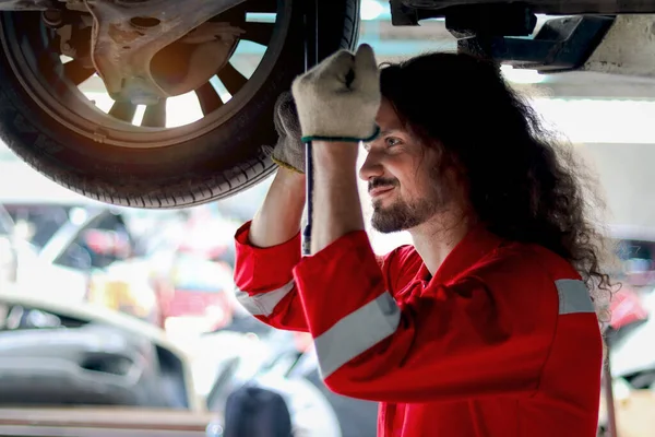 Długie Włosy Przystojny Mechanik Człowiek Czerwonym Mundurze Pracy Podnoszonym Pojazdem — Zdjęcie stockowe