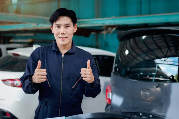 亚洲英俊的机械师 身穿制服 高举大拇指对着相机 汽车修理工 修理引擎 顾客汽车 在汽车修理店里的形象 — 图库照片