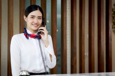 Güzel gülümseyen Asyalı kadın resepsiyonist resepsiyondaki müşteriyle konuşuyor. Bayan personel tatil için otel rezervasyonuna yardım ediyor..