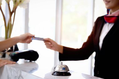 Otel resepsiyon masasındaki gümüş zil. Kadın resepsiyonist elinin bulanık geçmişiyle otelden, hizmet otelinden ve ödeme konseptinden kredi kartı almak için elini uzatıyor..