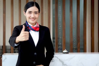 Mutlu gülümseyen, siyah takım elbiseli güzel Asyalı kadın resepsiyonistin portresi otel resepsiyonundaki kameraya çarpıyor, tatilde otel servisini kontrol ediyor..
