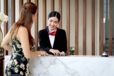 Güzel gülümseyen Asyalı resepsiyonist, turist kadın müşteriler için seyahat programı, resepsiyondaki kadın çalışanlar için bilgi, tatil gezisi için otelde misafir rezervasyonu öneriyor..