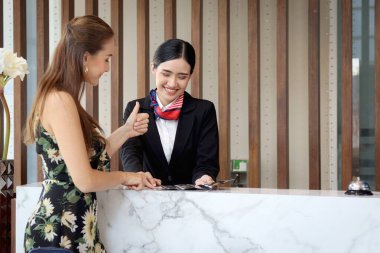 Güzel gülümseyen Asyalı resepsiyonist, turist kadın müşteriler için seyahat programı, resepsiyondaki kadın çalışanlar için bilgi, tatil gezisi için otelde misafir rezervasyonu öneriyor..