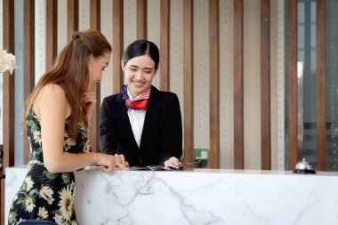 Güzel gülümseyen Asyalı resepsiyonist, turist kadın müşteriler için seyahat programı, resepsiyondaki kadın çalışanlar için bilgi, tatil gezisi için otelde misafir rezervasyonu öneriyor..
