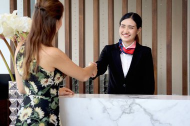 Mutlu gülümseyen, siyah takım elbiseli güzel Asyalı kadın resepsiyonist otel resepsiyonunda müşteri ziyaretçisini selamlıyor, tatil için otel servisine bakıyor..